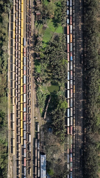 Chattogram, Bangladesh - 26 February 2025: Aerial view of the rail yard with rows of colorful freight train cars, lush green vegetation, palm trees, and a small pond between the tracks.