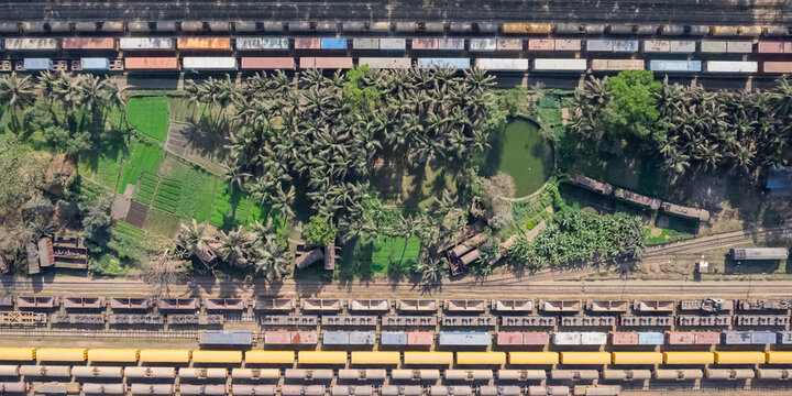 Chattogram, Bangladesh - 26 February 2025: Aerial view of the rail yard with rows of freight train cars, lush palm trees, and small green agricultural plots.