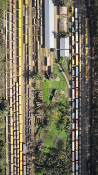 Chattogram, Bangladesh - 26 February 2025: Aerial view of the busy rail yard with numerous freight train cars parked on parallel tracks, adjacent to green agricultural fields and lush vegetation.