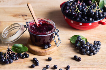 Homemade aronia berry jam in an open glass jar with fresh black chokeberries on a wooden table. Organic homemade food, seasonal harvest and superfood concept. © Melica