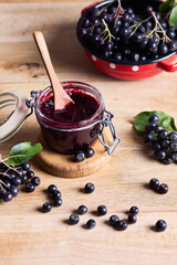 Homemade aronia berry jam in an open glass jar with fresh black chokeberries on a wooden table. Organic homemade food, seasonal harvest and superfood concept. © Melica