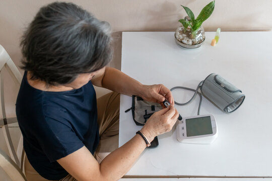 Senior Asian Woman Preparing Blood Glucose Meter for Self-Monitoring at Home