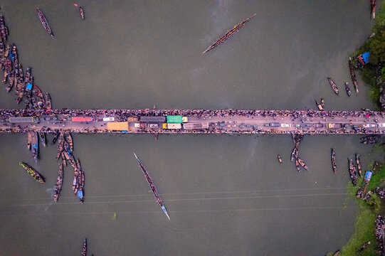 Sirajganj, Rajshahi, Bangladesh - 19 September 2025: Aerial view of traditional boat race with wooden boats navigating the river under a bridge crowded with spectators.