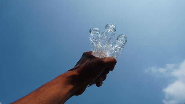 A low perspective captures the hand gripping the crushed plastic bottles against the blue backdrop