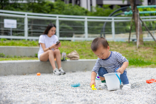 Toddler playing with bucket in gravel pit near mother