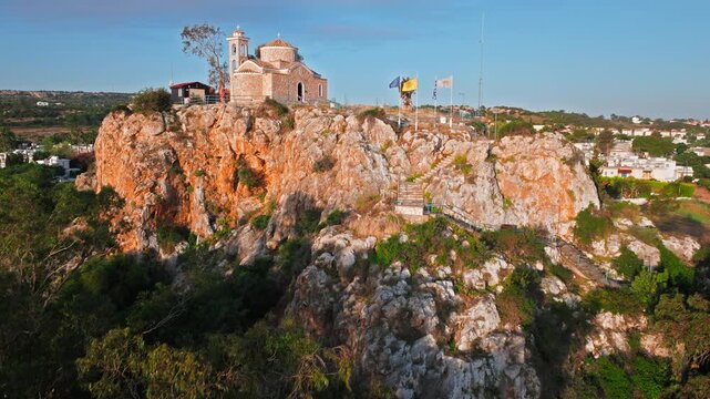 Drone view of Profitis Elias Church in Protaras, Cyprus. The small stone chapel sits on a dramatic rocky hilltop overlooking the Mediterranean landscape.