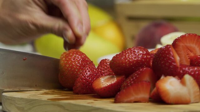 Cook slicing up strawberry and putting it with others - closeup, slow motion