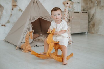 a child is riding a wooden horse in a children's room near a teepee, a children's room in a house © Any Grant