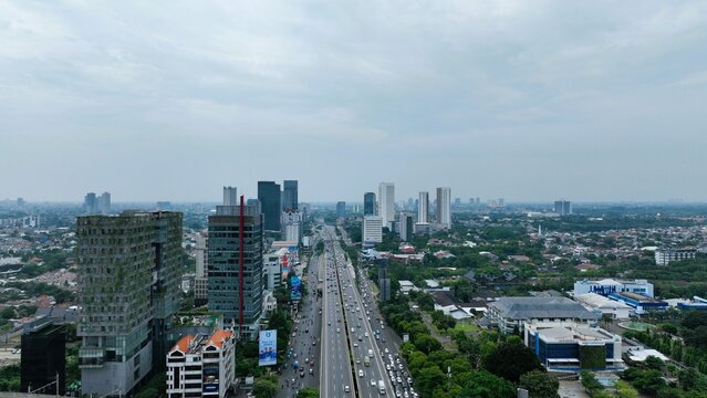 Cilandak, Indonesia - 04 May 2025: Aerial view of the Jakarta Outer Ring Road highway with surrounding high-rise office buildings, dense urban greenery, and traffic under a cloudy sky.
