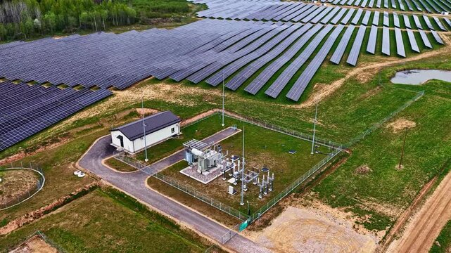 Aerial view of a large solar farm with rows of photovoltaic panels and a small electrical substation in Latvia.