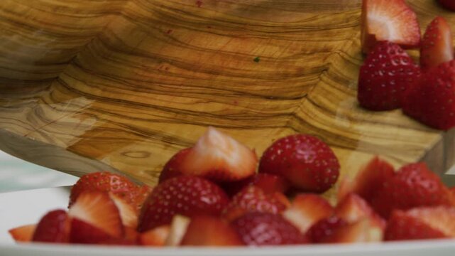 Slow motion shot of knife scrapping strawberries off wooden cutting board