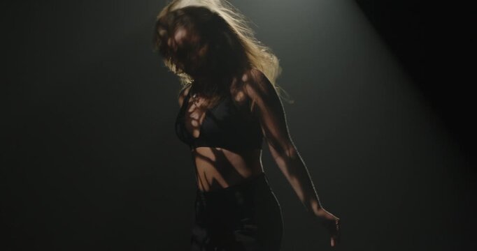 Silhouette of a female dancer performing under a single dramatic overhead spotlight on a dark stage. Concept of dance, performance, nightlife and art, fitness, fashion and entertainment advertising.
