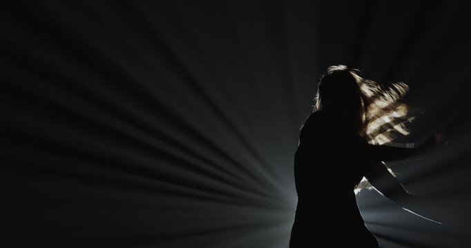 Silhouette of a female dancer performing on a dark stage, back lit by dramatic volumetric light rays with copy space. Concepts related to dance, self discovery, album covers, singles, or podcasts