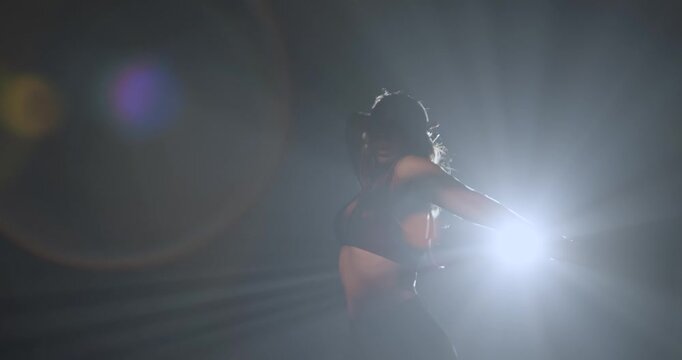 Backlit woman dancing on dark stage with lens flare. Concept of abstract artistic performance for music album cover, theater promotion and creative advertising backdrop design.
