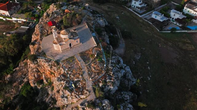 Aerial view above Profitis Elias Church in Protaras, Cyprus. The stone chapel, rocky hill and surrounding resort area create a scenic coastal panorama.
