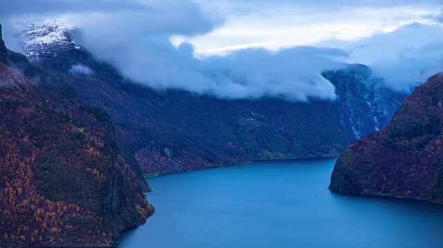 View of Aurlandsfjord surrounded by steep mountains with low hanging clouds and deep blue waters in Flam, Vestland, Norway.