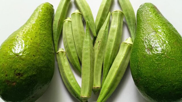 Fresh raw green okra Abelmoschus esculentus pods in heart shape flanked by two whole avocados Persea americana isolated on clean white background in Guatemala