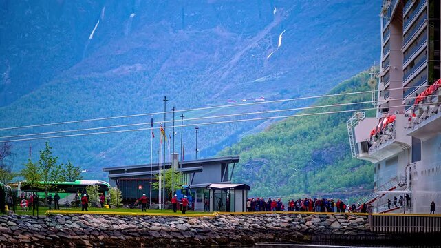 View of a large cruise ship docked at the port in Flam with passengers disembarking near the scenic fjord mountains in Flam, Vestland, Norway.