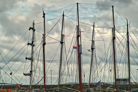 Tall ship masts and intricate rigging forming a nautical pattern against a dramatic sky, displaying a colorful rainbow flag