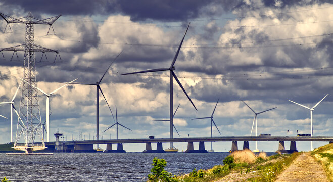 Wind power generation and electricity transmission lines stretching across ketelbrug bridge under a cloudy sky