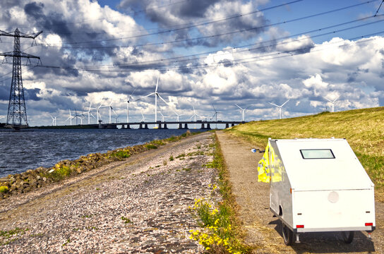 Bicycle caravan on dike path traveling past wind turbines and power lines under dramatic sky