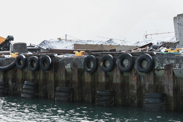 Obraz premium A snowy industrial harbor dock lined with tire fenders and yellow bollards, weathered rusted quay walls and cranes in the background, evoking maritime industry, cold season and urban decay