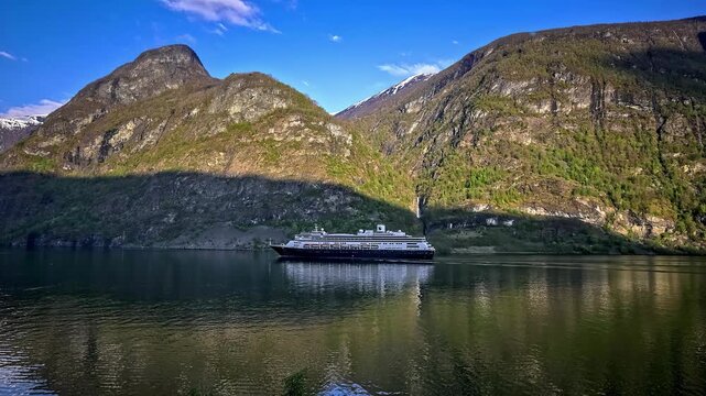 View of Flam fjord with towering mountains and a distant waterfall reflecting in the calm water in Flam, Vestland, Norway.