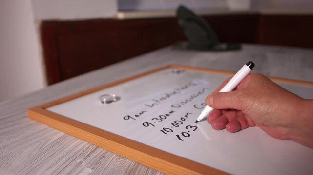 Hand writing out meeting schedule on whiteboard