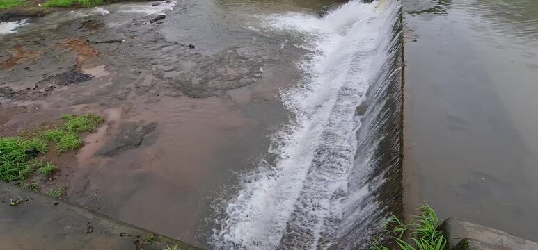 Rainwater Gushing Over Concrete Check Dam Wall Creating Cascade Waterfall in Rural Riverbed During Monsoon