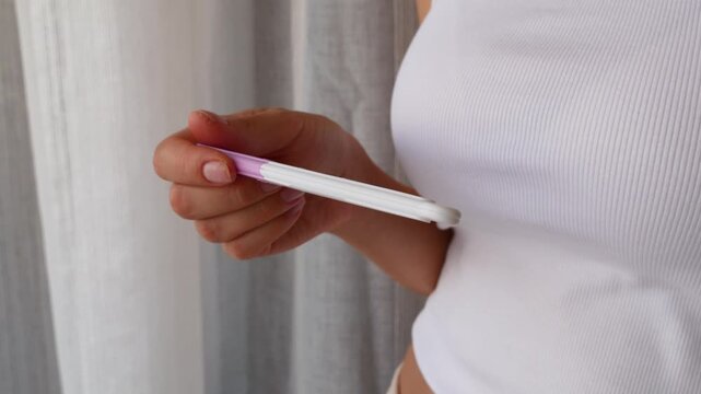 Woman holding home pregnancy test during early pregnancy check.