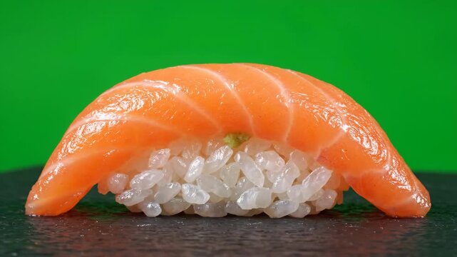 Detailed close up shot of a fresh salmon nigiri sushi rotating slowly on a flat surface against a bright green screen background for chroma key