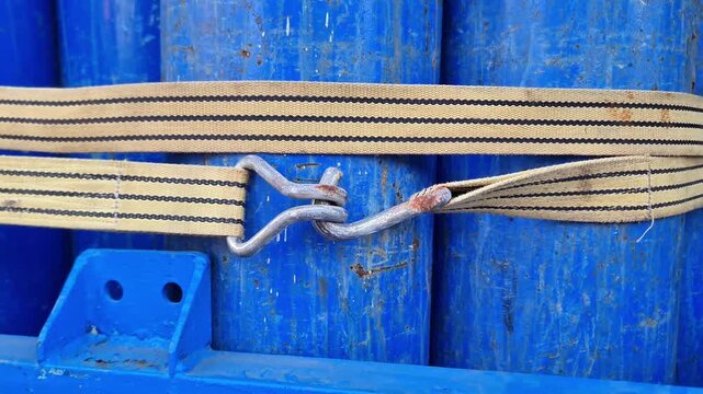 Close-up of heavy-duty tie-down strap and metal hook securing stacked blue steel pipes on a truck bed