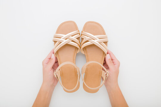 Young adult woman hands holding and showing new light brown female sandals with straps on light gray table background. Closeup. Point of view shot. Top down view.