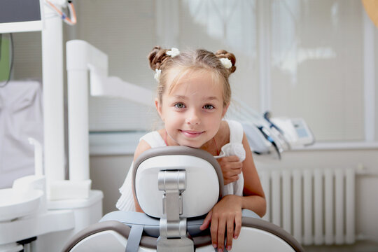 Happy little girl smiles while sitting in dental chair in bright clinic. Positive portrait of small pediatric dentistry patient. Image is perfect for advertising pediatric dentistry
