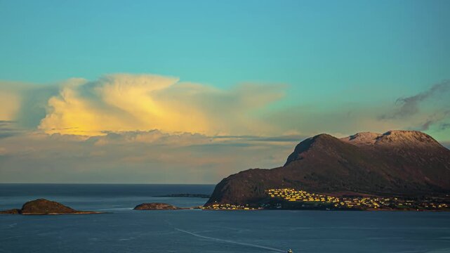View of coastal landscape with mountains, sea, and a small town at sunset in Alesund, More og Romsdal, Norway.
