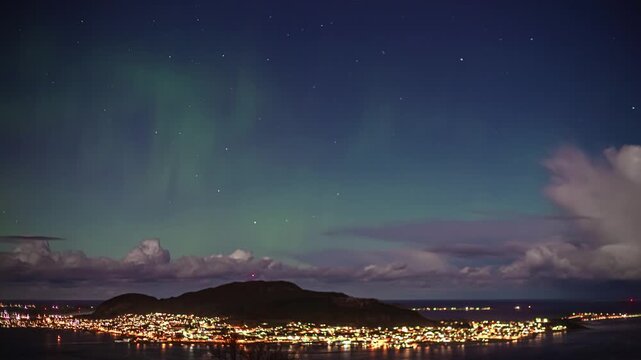 View of the aurora borealis illuminating the night sky above the illuminated city of Alesund, More og Romsdal, Norway.