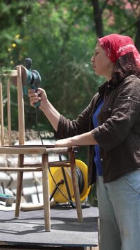 Woman Using an Electric Sander to Restore an Old Wooden Chair: DIY Furniture Renovation and Sustainable Upcycling