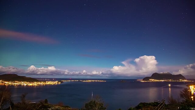 View of the illuminated coastal town of Alesund at night with starry sky and mountains in the background in Alesund, More og Romsdal, Norway.