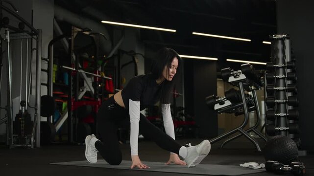 Athletic Caucasian woman female fitness trainer doing yoga pilates stretching exercise in dark gym sportswoman athlete training legs muscles on mat workout routine sport equipment flexibility practice