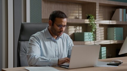 Fototapeta premium Tired exhausted Indian Arabian business man holding head headache closing laptop after work office businessman male worker feeling fatigue eyes strain employer finishing online task indoors workplace