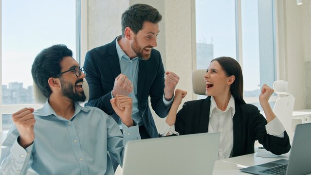 Happy multiethnic business team work laptop celebrating success inside office sales win corporate teamwork excited smiling businessmen businesswoman colleagues working computer documents data finance