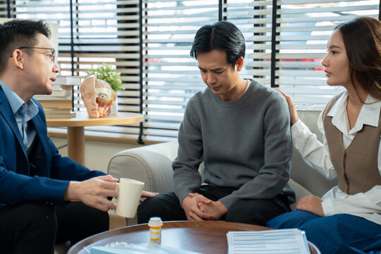 Young Asian couple sitting on sofa and talking with a professional therapist at clinic.Family therapy,Marriage,depression support,counselling,anxiety therapy,trauma advice,marriage help,mental health