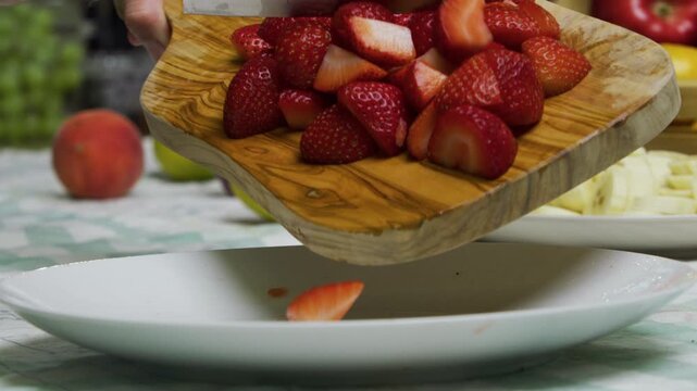 Diced strawberries rolling off chopping board onto plate in slow motion