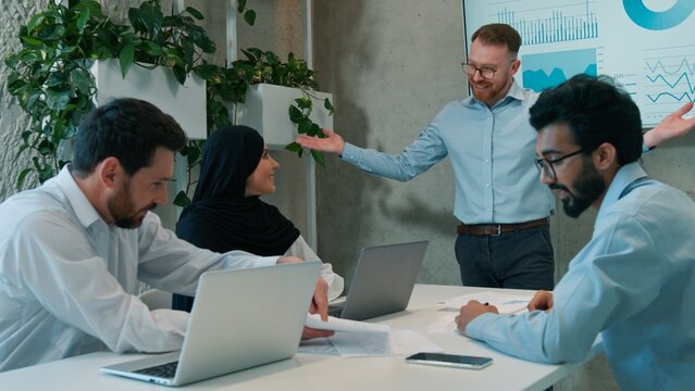 Multiracial business team men muslim businesswoman celebrating success presentation indoor meeting discussing sales graphics results diverse ethnic office colleagues investors teamwork strategy profit
