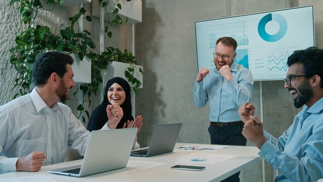 Happy multiethnic diverse business partners celebrating victory office ethnic Arabian Indian businessmen muslim businesswoman achieving successful deal laptop computer teamwork result indoor boardroom