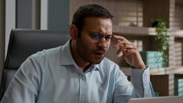 Angry frustrated Indian American business man throwing papers desk stressed worker with laptop tired unhappy male businessman office employee deadline paperwork problem burnout hate trouble hard work