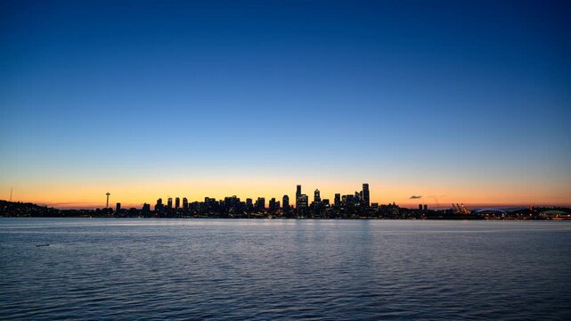 View of the Seattle skyline illuminated against a vibrant sunset sky over the calm waters of Elliott Bay in Seattle, Washington, United States.