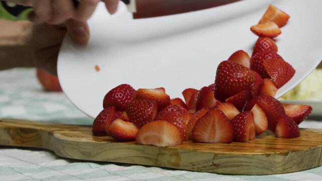 Cook moving diced strawberries back and forth from chopping board to plate in slow motion