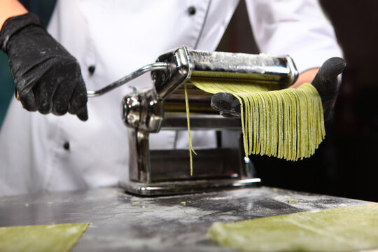Pasta making machine and dough rolling. Chef makes dough with spinach. Homemade pasta. Making pasta with spinach. Paste is green