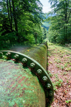 View of the historic penstock of the Jasenie Hydroelectric Power Plant stretching through a lush green forest in Jasenie, Banska Bystrica Regio, Slovakia.